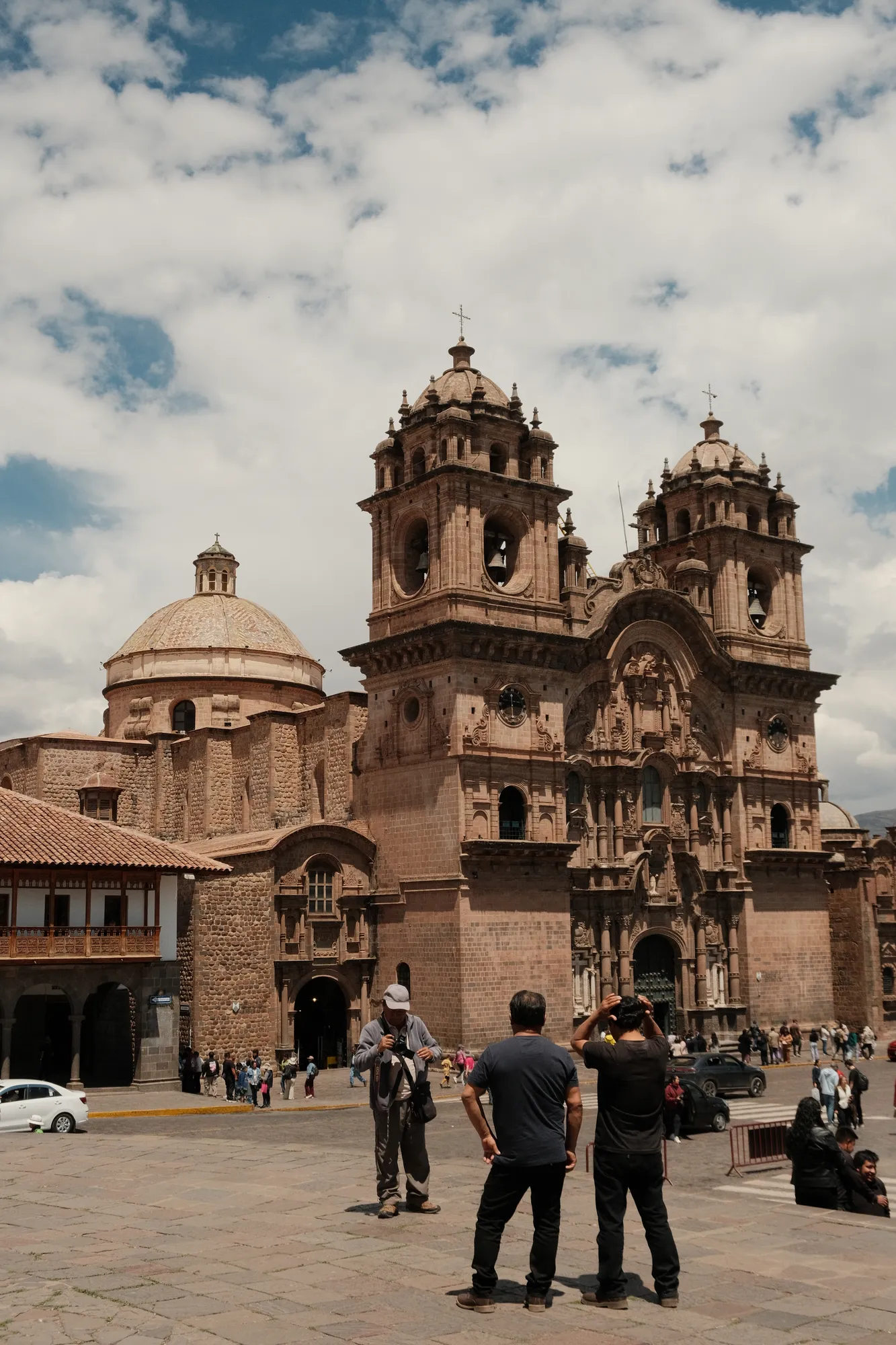 The Church of the Compañía de Jesús fills Cusco's Plaza de Armas, its carved stone facade and twin bell towers against a cloudy sky.