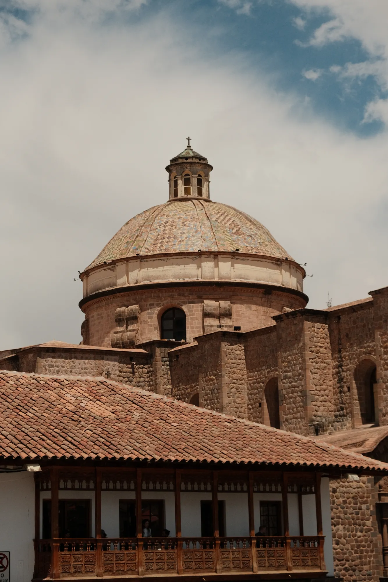 A tiled colonial dome with a small bell tower rises above a wooden balcony in Cusco.
