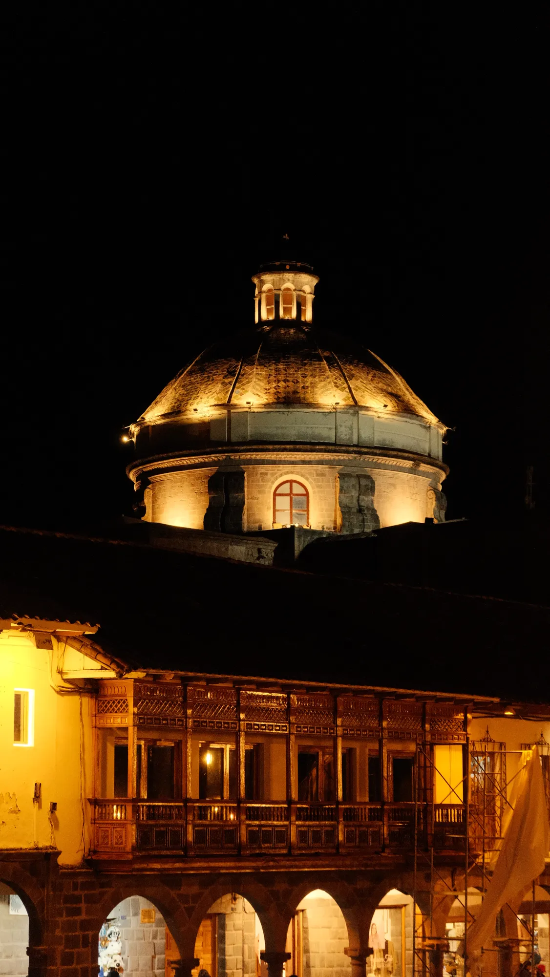 A colonial church dome glows at night above an arcaded balcony on Cusco's Plaza de Armas.