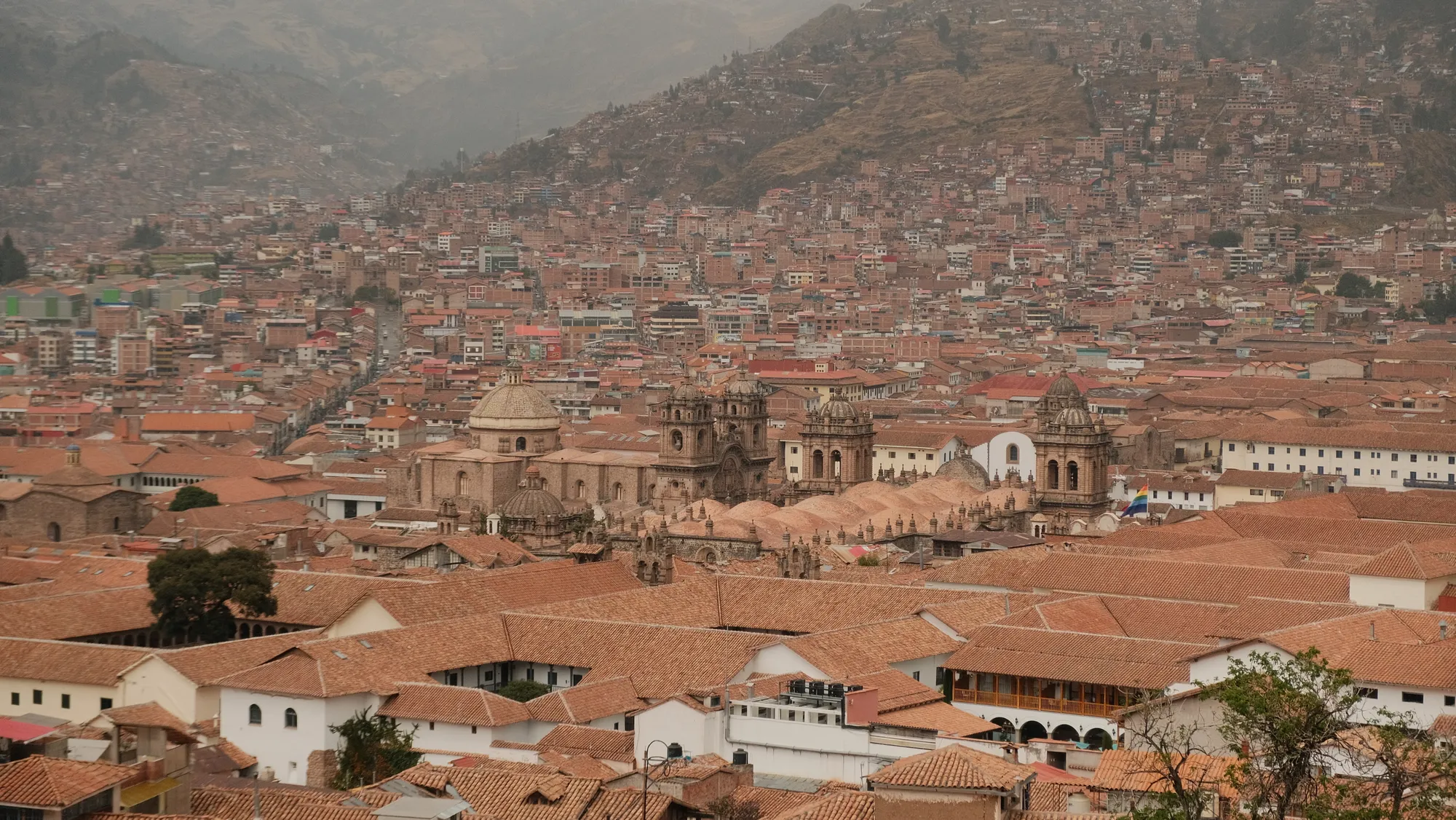 Cusco's Plaza de Armas and cathedral domes seen from above, the city spreading up the surrounding hillsides.