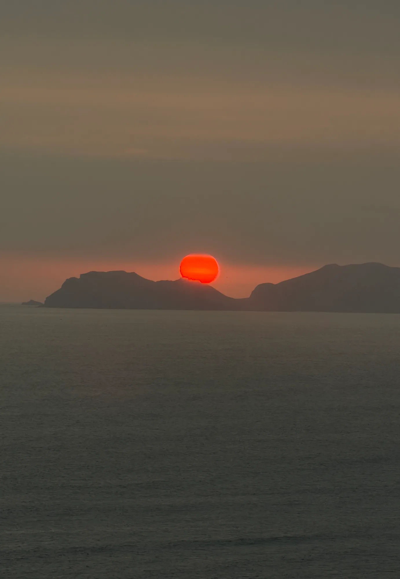 The sun sets as a full orange disc over the Pacific, silhouetting the headlands south of Lima.