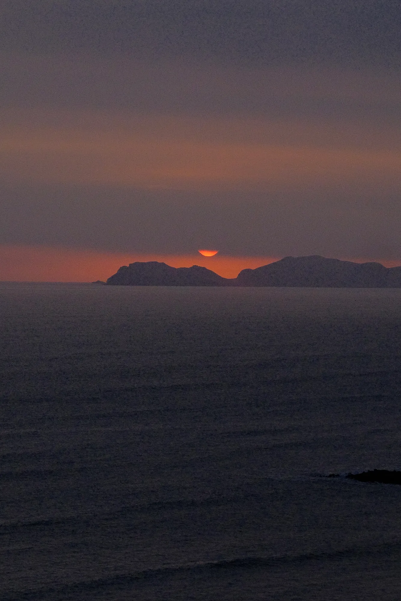 Dusk settles over the Lima coastline as the last curve of the sun disappears behind the headland.
