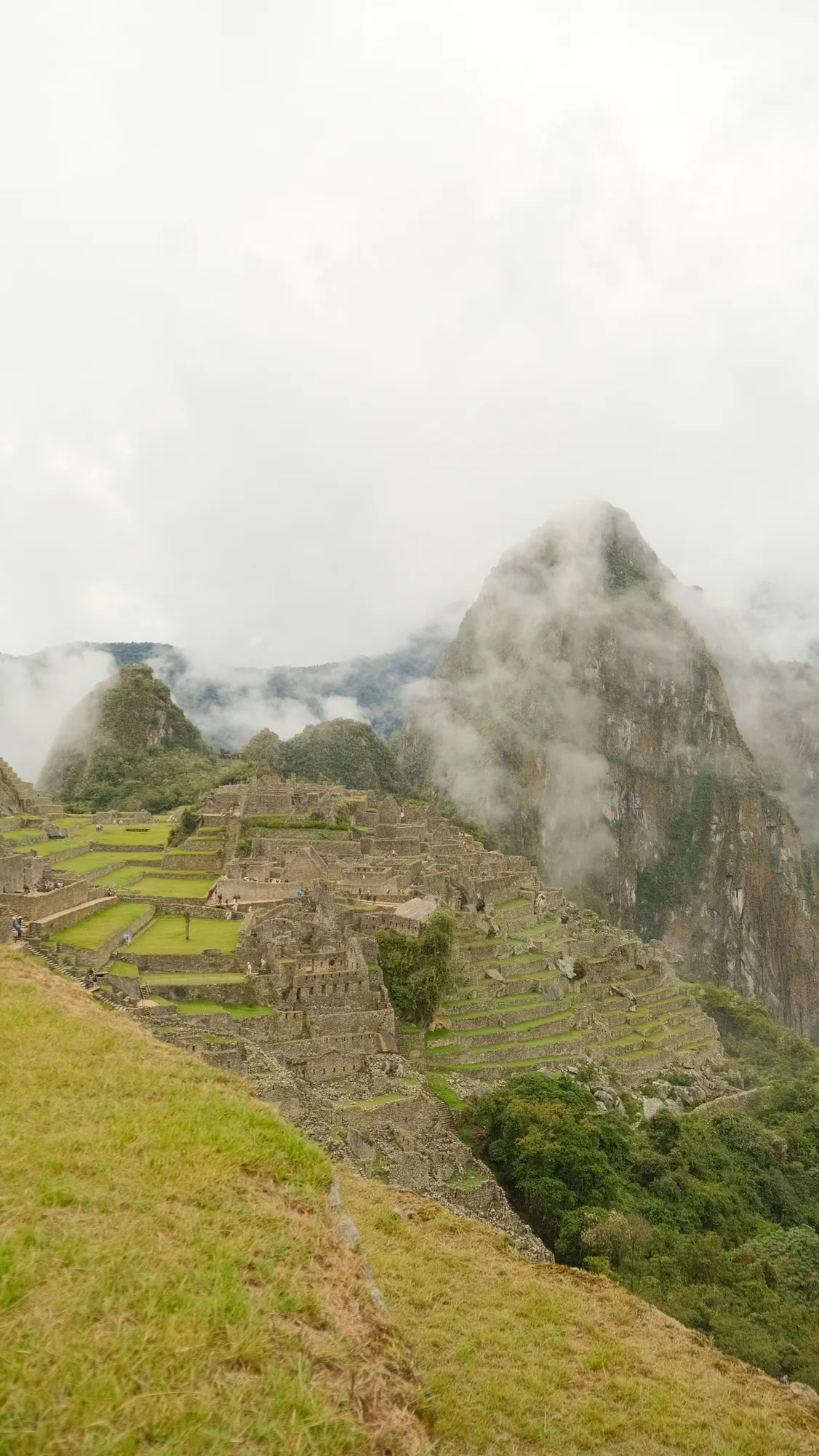 Machu Picchu's ruins seen from a higher vantage point, mountains rising behind.