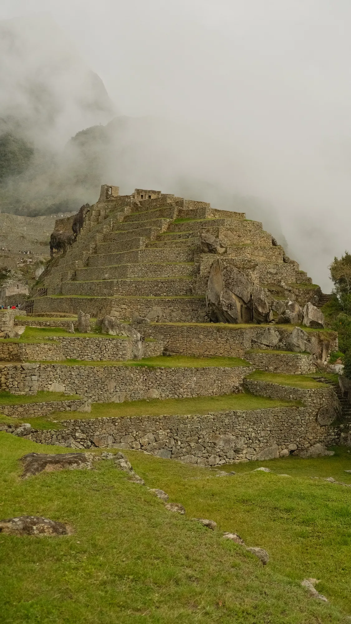 Machu Picchu's stone structures under a partly clouded sky, afternoon.