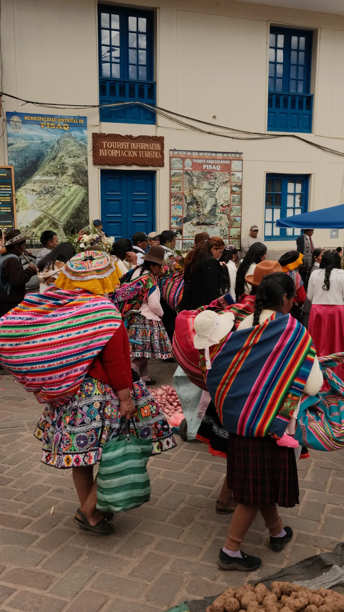Onlookers and wedding guests gather in Pisac's plaza under market awnings.