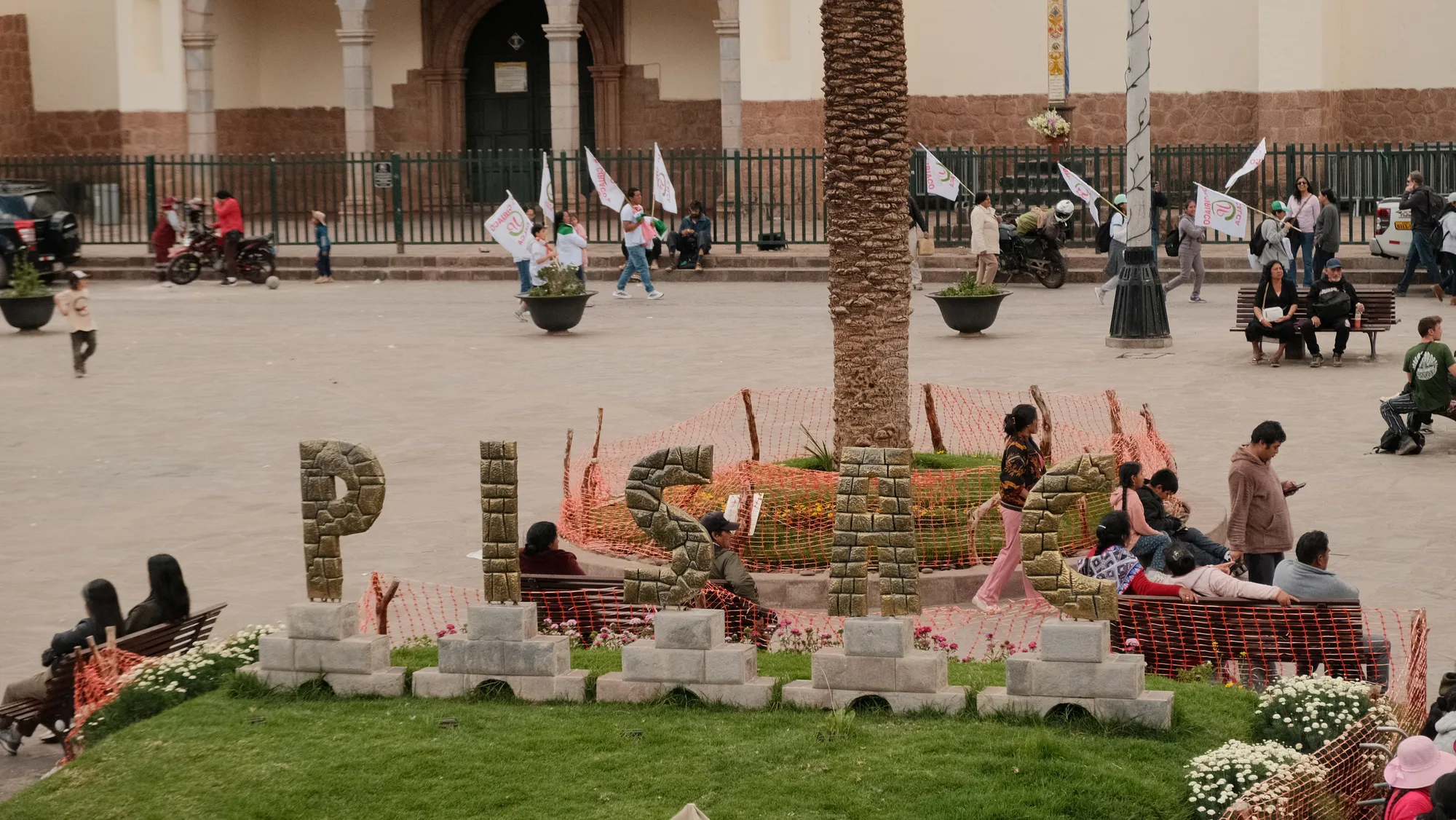 A painted mural building and craft stalls in Pisac's plaza, mountains rising behind the town.