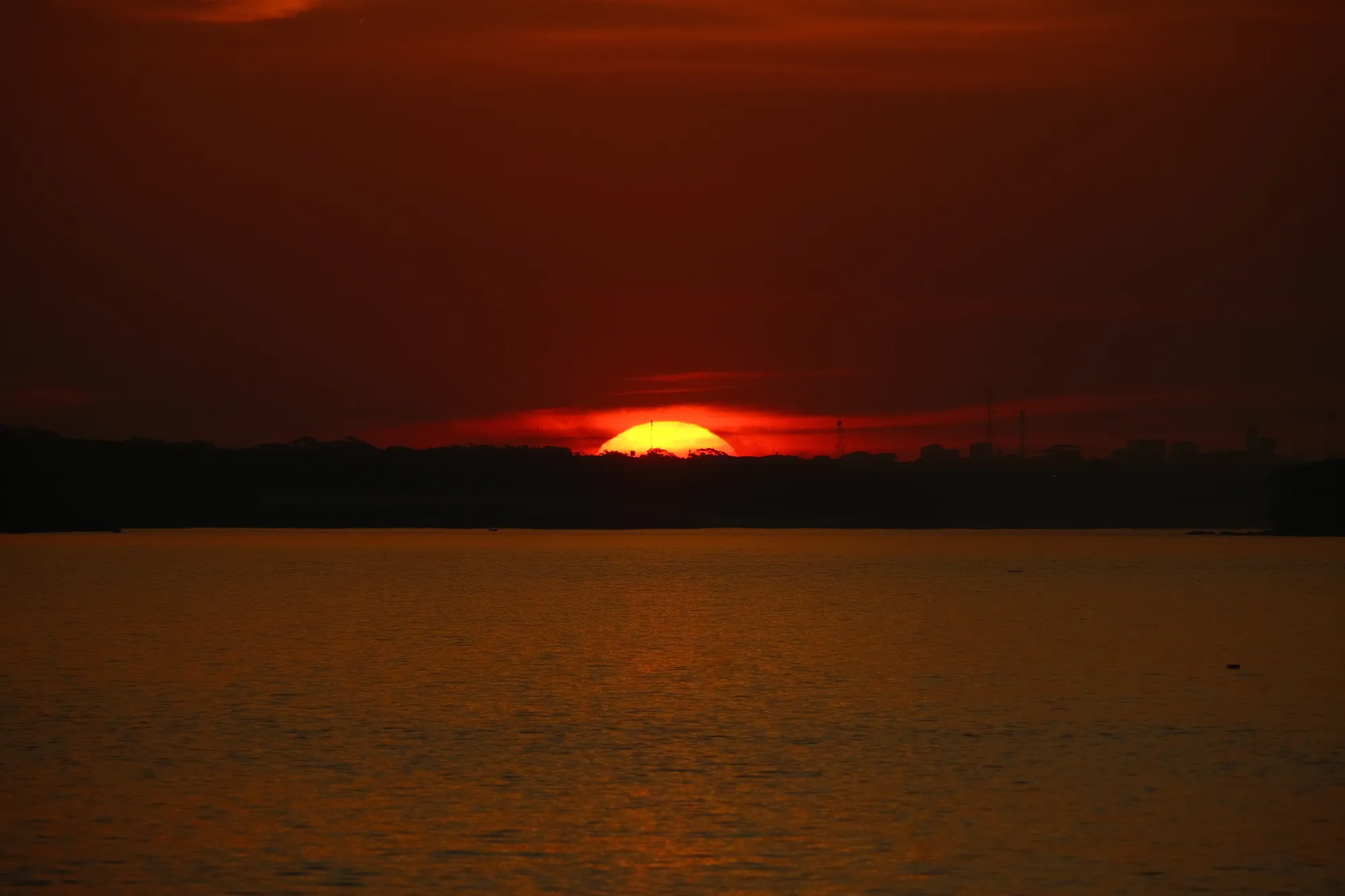 The sun sets in deep red and gold over a river near Puerto Maldonado, the forest silhouetted along the far bank.