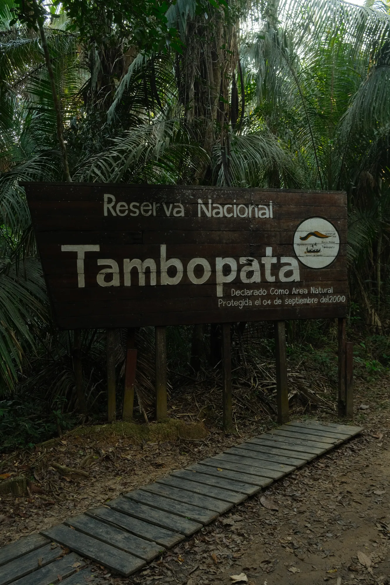 A wooden sign for the Tambopata National Reserve marks the trailhead into the rainforest.