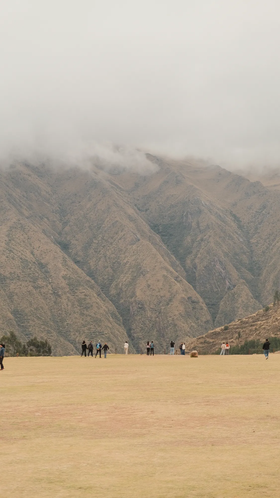 Visitors look out over the valley from a grassy overlook near Chinchero, cloud-wrapped mountains rising beyond.
