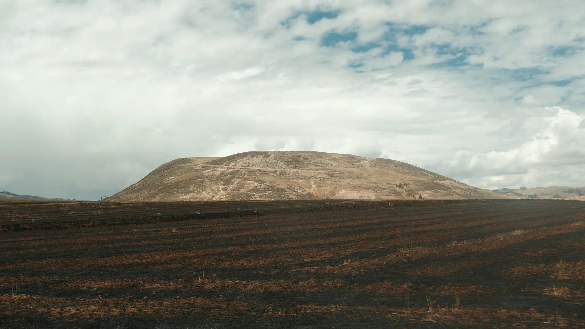 A freshly burned field lies before a bare hillside in the Sacred Valley, a common sight during land preparation between seasons.
