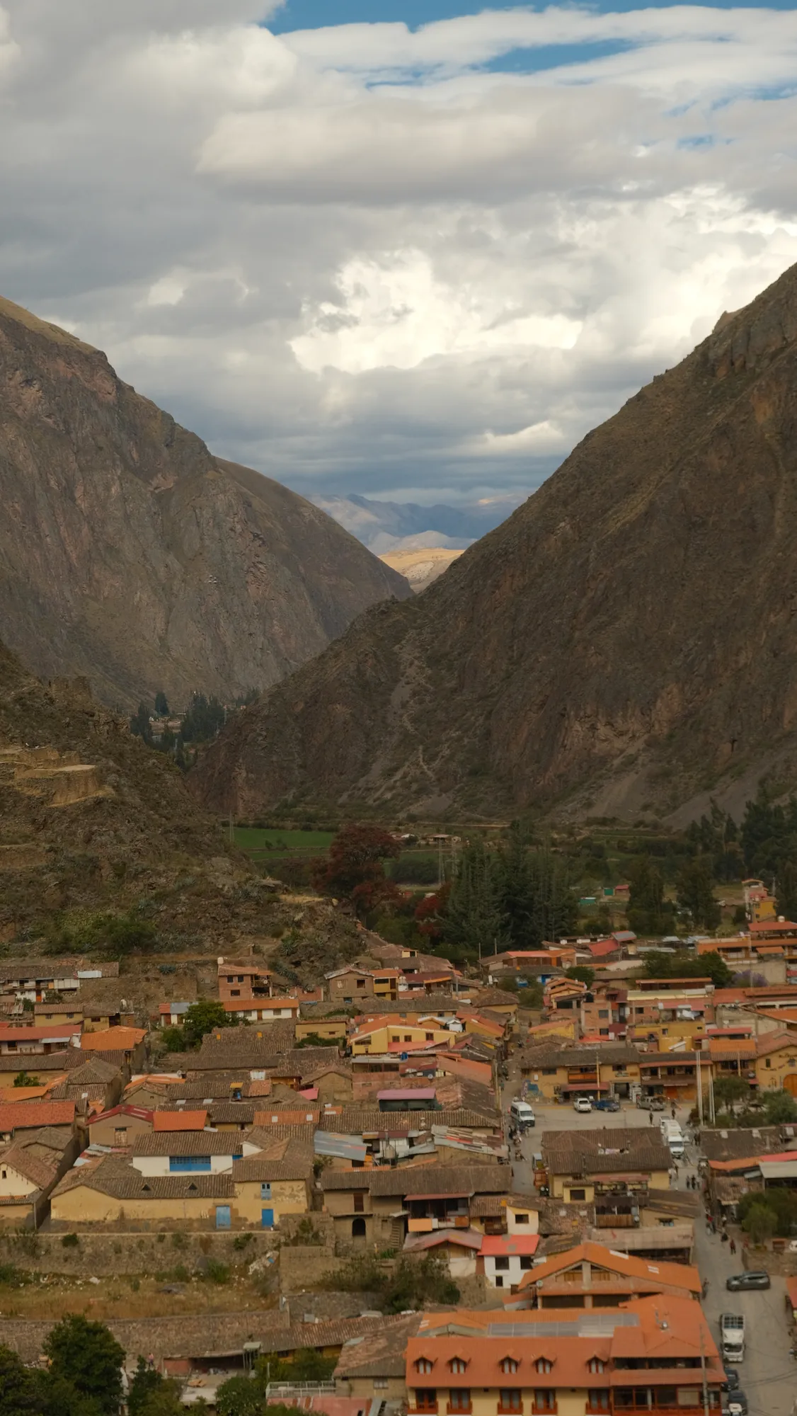 The town of Ollantaytambo fills a narrow valley between steep Andean peaks, terracotta roofs and Inca terracing visible on the hillside above.